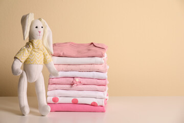 Stack of baby girl's clothes and toy bunny on white table. Space for text