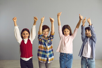 Energetic optimistic preteen children happily smiling show hands up with thumbs up gesture. Victory, confidence, success and approval concept. Studio portrait shot on grey copy space