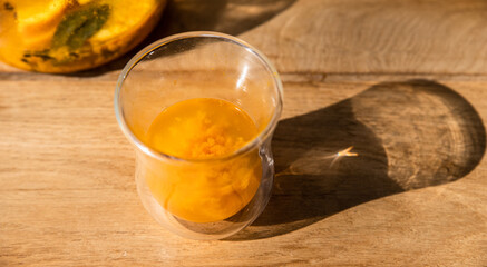 Glass cup with sea buckthorn tea and teapot on wooden table in cafe. Traditional autumn hot drink.