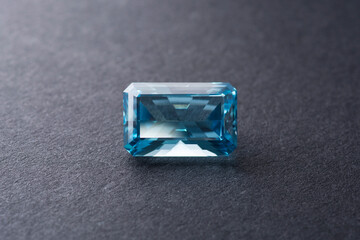 Natural London blue topaz. Emerald faceted, loupe clean - VVS,IF,FL. Heated treated, irradiated, color enhanced. Semiprecious gemstone in gray pattern gradient background. Counter side light.