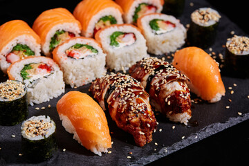 Close up of sushi sashimi with salmon, sesame and sauce on a black board.