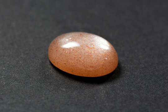 Loose natural oval cabochon sunstone gemstone light peach color with inclusions of hematite and copper in the mineral what gives a  golden shimmer. Isolated gem from feldspar family on gray background