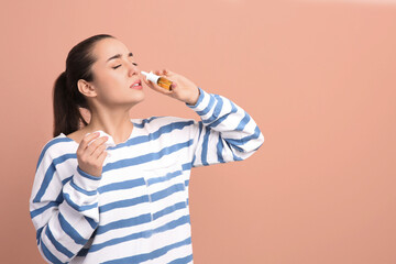 Woman using nasal spray on beige background, space for text