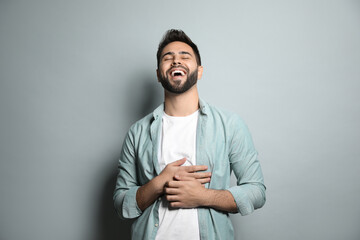 Young man laughing on light grey background. Funny joke