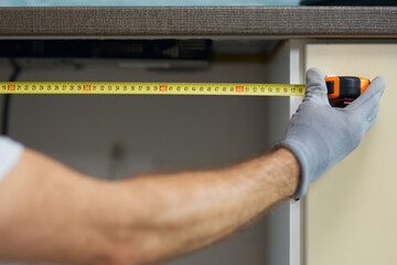 Close up of hand of young repairman, professional plumber using measure tape while doing plumbing...