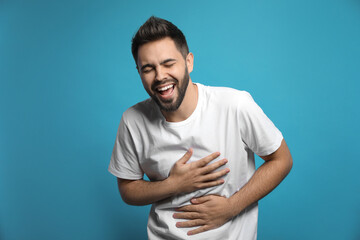 Young man laughing on light blue background. Funny joke