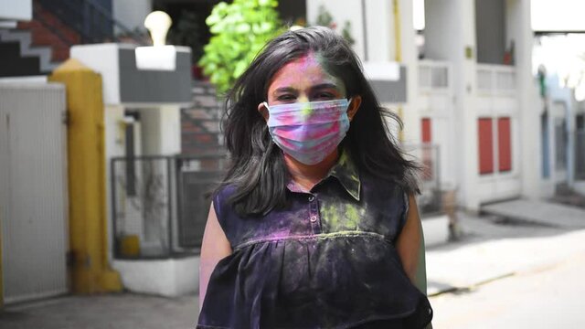 Portrait of young Indian woman covered with colors wearing protective mask during celebration of holi festival in 2021