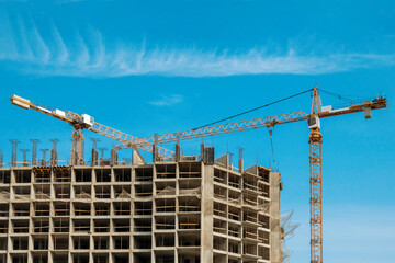 Two construction cranes against a blue sky background. Construction tower crane in yellow colour....