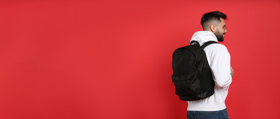 Young man with stylish backpack on red background, back view. Space for text - obrazy, fototapety, plakaty