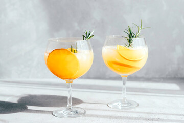 Glasses, glasses with a summer refreshing cocktail with orange and ice cubes and a sprig of rosemary in the rays of the bright sun