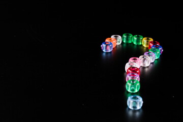 question mark made of colourful transparent beads, isolated on black background with copy space