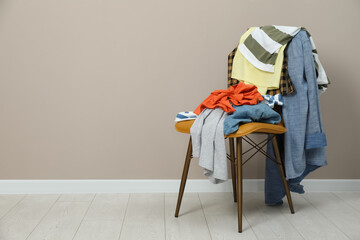 Different clothes on chair near light grey wall, space for text - obrazy, fototapety, plakaty