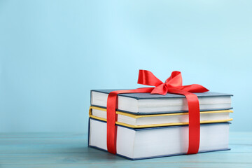 Different books tied with red ribbon on light blue wooden table, space for text