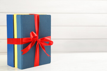 Different books tied with red ribbon on white table, space for text