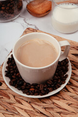 Cup with coffee with milk on a white plate full of natural coffee beans