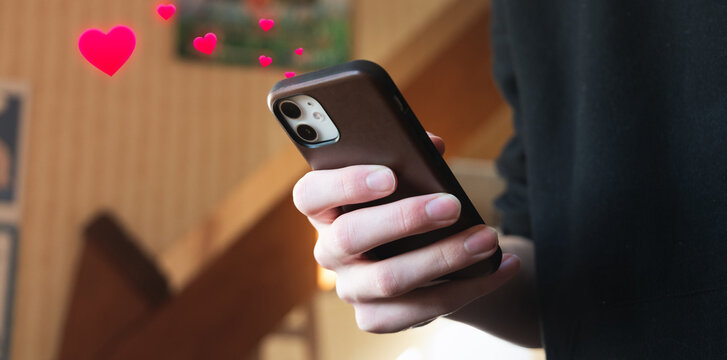 Jeune homme mettant des J'aime (likes sous forme de c&oelig;urs) sur son t&eacute;l&eacute;phone portable, sur un r&eacute;seau social