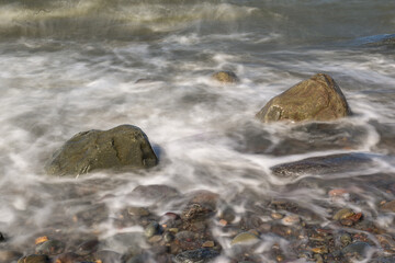 Looking out over a calm blue ocean view of shoreline with sea waves crashing on rocks