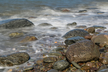 Looking out over a calm blue ocean view of shoreline with sea waves crashing on rocks