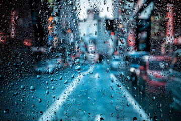 Beautiful landscape conceptual view of the city through glass window with raindrops. Rain at urban night view of the city.