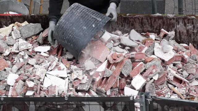 bricklayer worker in construction site depositing rubble in container for pickup by truck , video hd footage