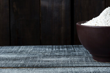 Heap of wheat flour in a plate on a wooden black background with copy space. banner