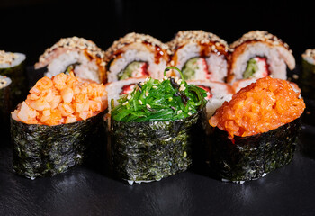 Sushi rolls with seaweed, shrimp, salmon and sprinkled with sesame seeds on a black board.