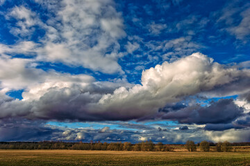 Fototapeta na wymiar Spring landscape. Dramatic clouds are floating over the field before sunset 