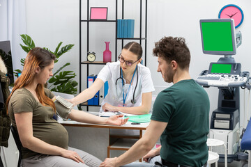 A gynecologist puts a blood pressure measuring device on a pregnant woman's arm. Green screen