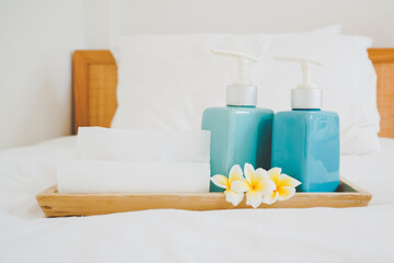 Fototapeta na wymiar bath accessories in blue ceramic bottles and blossom plumeria flower on wooden tray and hygiene comfortable bed in bedroom for spa ,recreation , hotel ,resort ,welcome guest concept