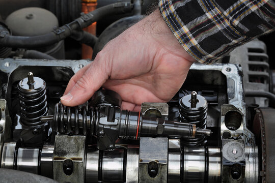 Car mechanic fixing modern diesel engine, closeup of hand holding injector with cylinder head and engine in background