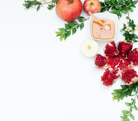 Creative layout of traditional symbols for jewish holiday - pomegranate, green branch, apple and cup with honey on white background. Concept Rosh Hashanah tova jewish New Year. Banner, fresh fruits