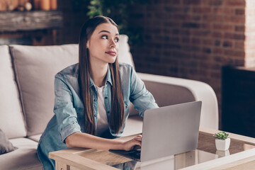 Photo of dreamy bored young woman sit sofa work from home look away laptop indoors inside house flat