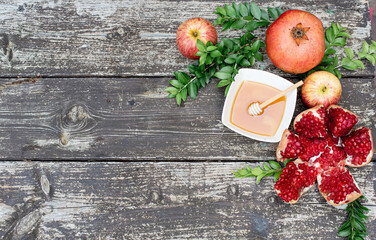Creative layout of traditional symbols for jewish holiday - apples, cup with honey, pomegranate, green branch on wooden background. Concept Rosh Hashanah tova jewish New Year. Banner, fresh fruits