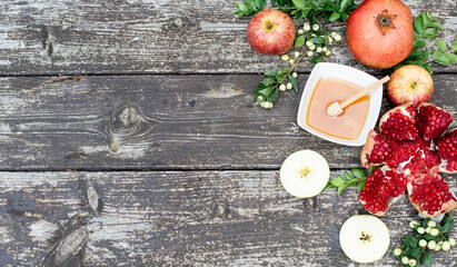 Beautiful layout of traditional symbols for jewish holiday - apples, cup with honey, pomegranate, green branch on wooden background. Concept Rosh Hashanah tova jewish New Year. Banner, fresh fruits