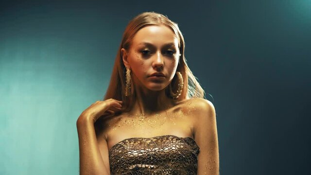 Portrait Closeup Beauty fantasy woman, face, body in gold paint. Golden shiny skin. Fashion model blonde girl. Glamorous earrings, ring jewellery accessories. Professional metallic glitter makeup