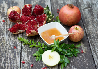 Creative layout of traditional symbols for jewish holiday-cup with honey, open pomegranate, apples on wooden background. Concept Rosh Hashanah tova jewish New Year. Side view, copy space, fresh fruits