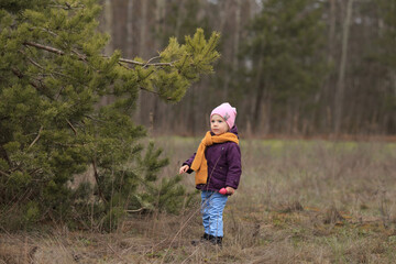 a girl with a knitted orange scarf stands in the woods and looks away
