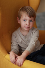 Naklejka premium Little blond boy on the yellow armchair. International Children's Day