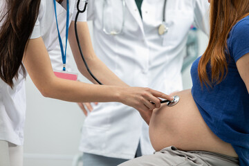 Close-up view of a lady doctor auscultating a pregnant woman's abdomen with a stethoscope....