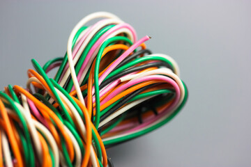 A bundle of multicolored electrical, car, computer, telephone wires twisted together background. Orange, green, pink, white cables on grey background . Computer networks, electrician services concept.