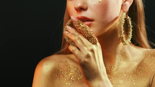 beauty fashion model girl's mouth close-up. Golden body skin. Glamour golden bright color. gold metal hand, finger touches juicy lips. Beautiful artistic makeup shiny paint on woman face. Lady goddess