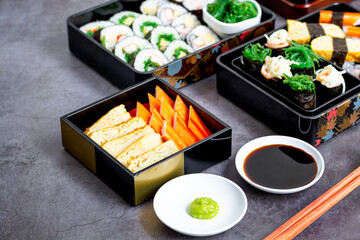 Set of variety sushi, Tamagoyaki, crabsticks sushi and maki in bento box served with soy sauce and wasabi. Delicious japanese food.
