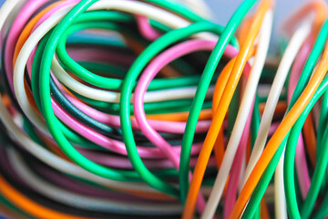 A bundle of multicolored electrical, car, computer, telephone wires twisted together background. Orange, green, pink, white cables on grey background . Computer networks, electrician services concept.