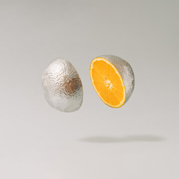 Sliced silver metallic orange fruit against gray background. Minimal cyberpunk or retro futurism fruit composition.