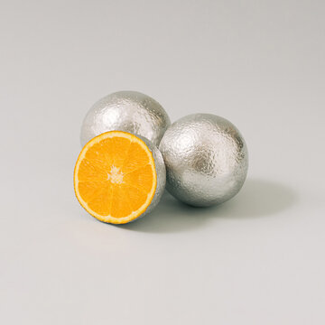 Sliced silver metallic orange fruit against gray background. Minimal cyberpunk or retro futurism fruit composition. Isomteric view.