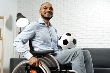 Happy young disabled man in wheelchair holding soccer ball and smiling