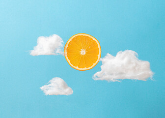 Orange fruit slice with soft white clouds on serenity sky blue background. Creative sunny summer day concept.