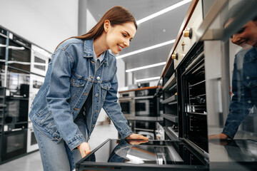 Young woman looking for new electric oven in a shopping mall