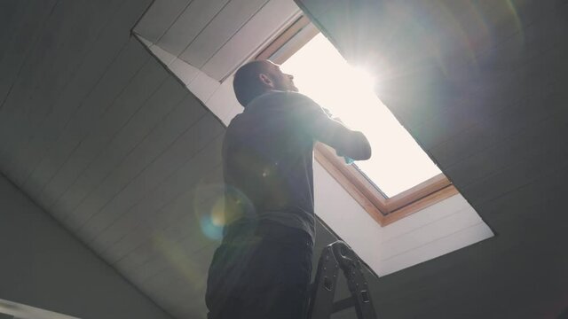 Caucasian man washes the attic window Bright sun illuminates the man in the window during the repair The husband performs finishing work in the house Happy family