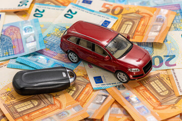 key and red toy car on pile of euro banknotes, buy or sell a car, rent a car or insurance concept